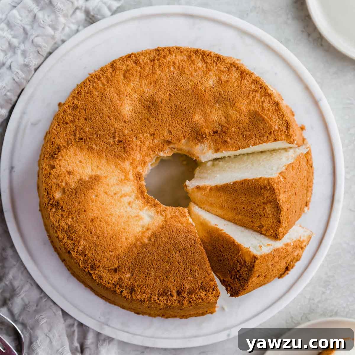 A baked angel food cake on a serving plate with two slices cut and laying on side, showing its light texture.
