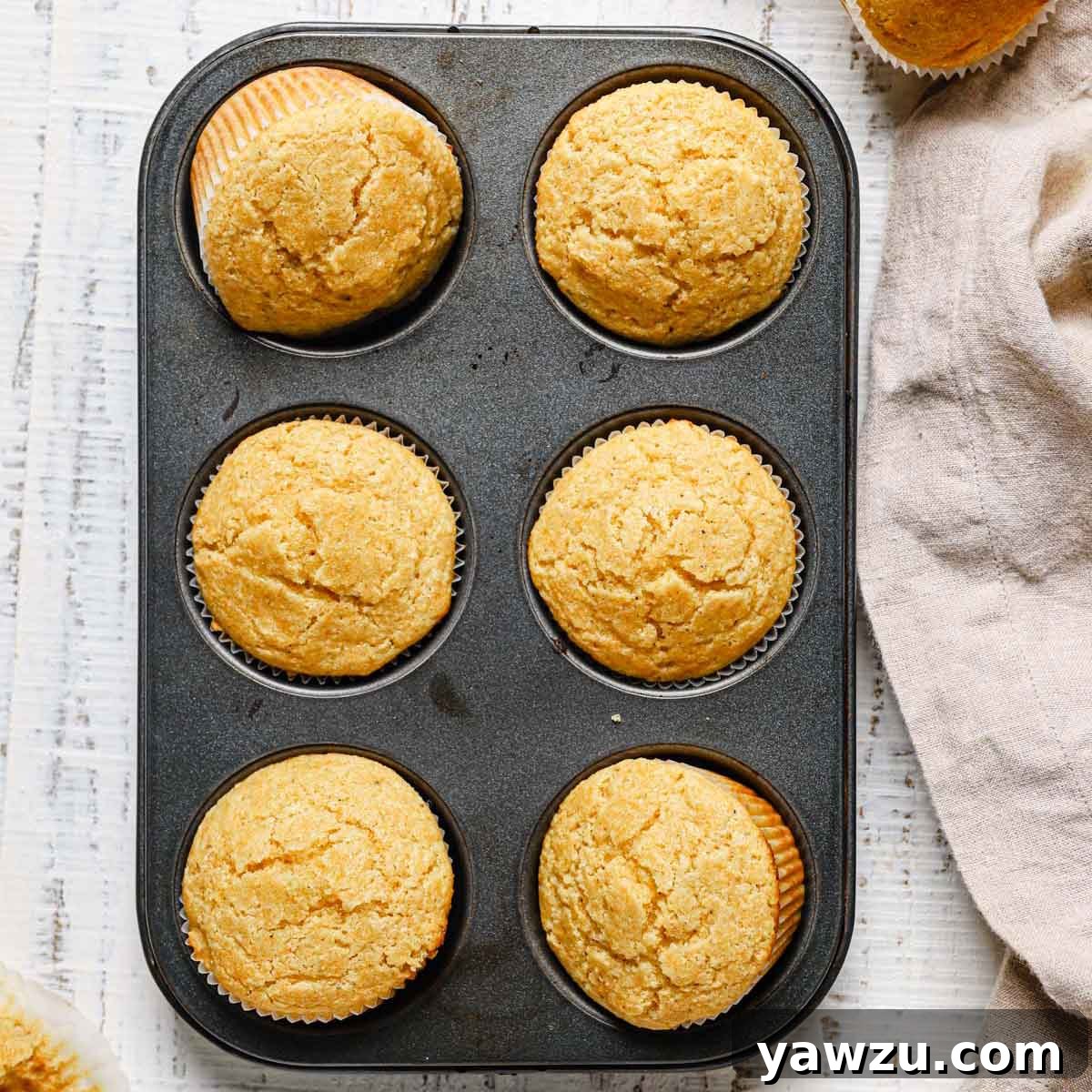 A stunning shot of golden cornbread muffins freshly baked in a pan, with two muffins playfully turned sideways to reveal their soft, inviting interior.