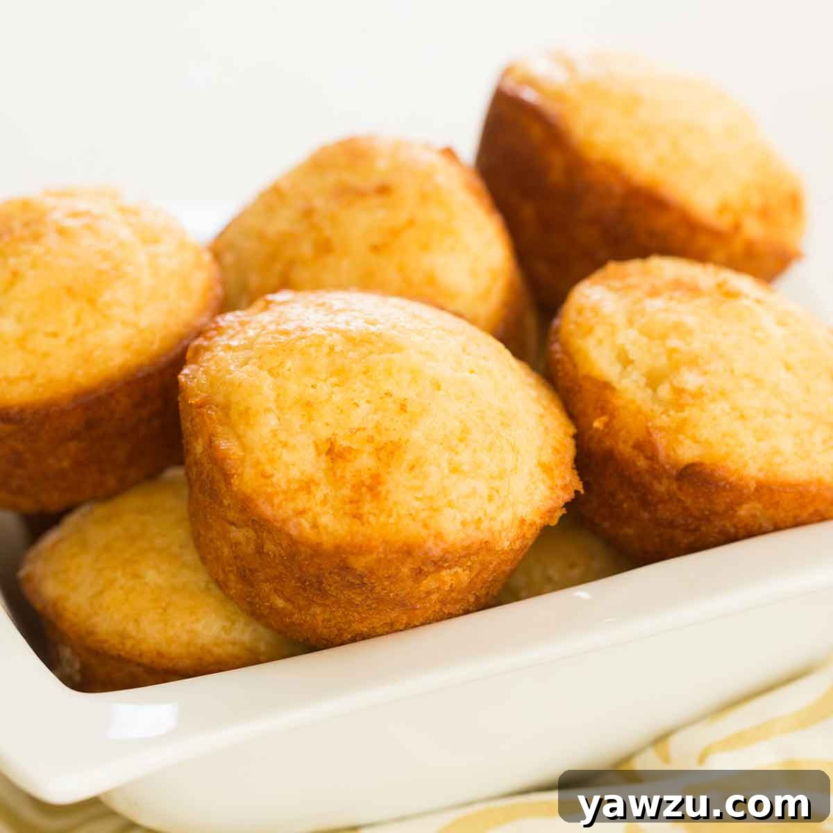 A generous batch of golden-brown honey muffins lovingly piled into a rustic white bowl, radiating warmth and home-baked goodness.