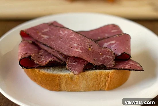 Thick slices of Italian bread topped with a generous portion of pastrami, ready for the next layer of a Primanti Bros. sandwich.