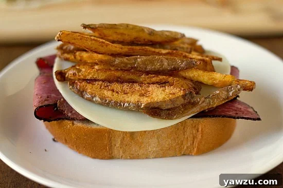 A generous handful of freshly made French fries piled high on top of the provolone cheese, a signature layer of the Primanti Bros. sandwich.