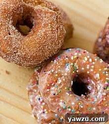 Overhead image of cinnamon sugar buttermilk doughnuts and glazed buttermilk doughnuts with nonpareil sprinkles on a wood surface.