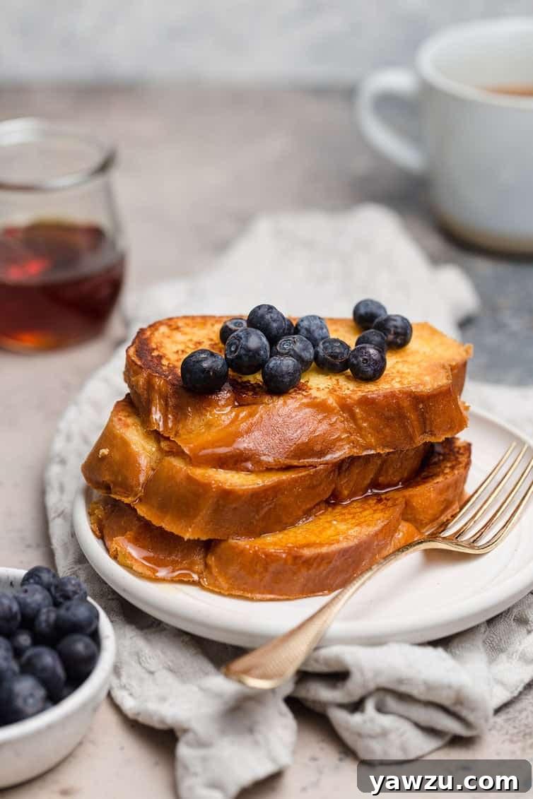 A stack of golden brown Challah French toast on a white plate with fresh blueberries on top, ready to be enjoyed.