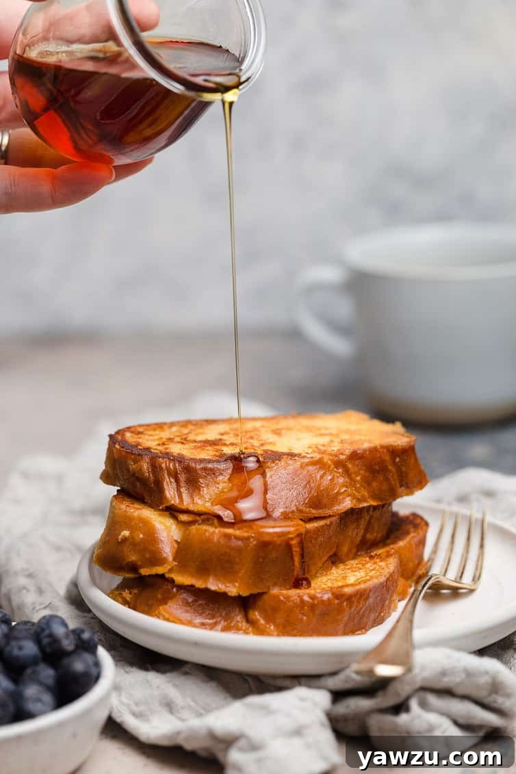 A beautifully stacked serving of Challah French toast, generously drizzled with golden maple syrup, ready to be eaten.