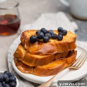A prepared plate of golden challah French toast with a side of syrup.