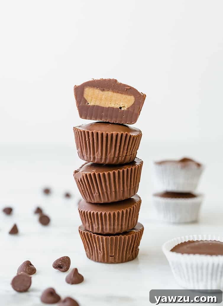 A stack of five peanut butter cups, with the top one sliced in half with filling exposed.
