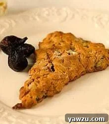 A honey fig scone on a white plate with dried figs as garnish.