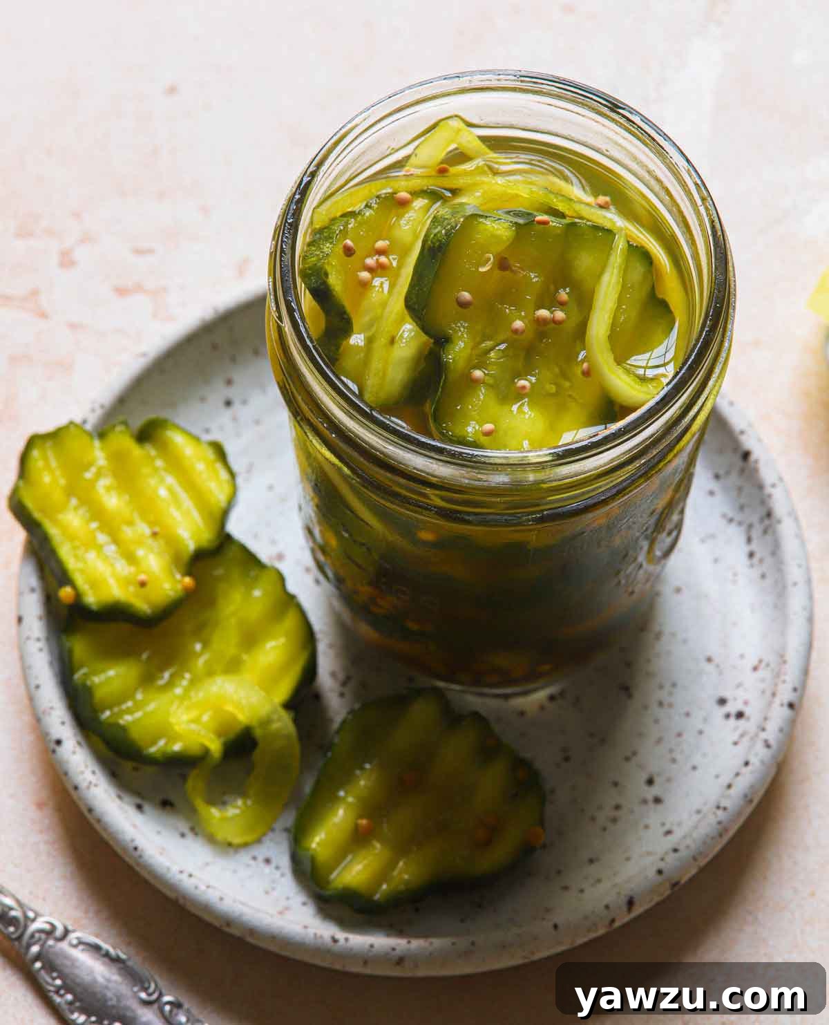 An open jar of golden-yellow bread and butter pickles, with three vibrant pickle slices arranged neatly on a small plate beside it, ready to be enjoyed.
