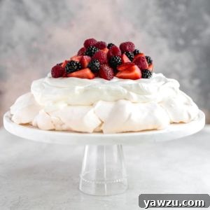 A slice of Pavlova on a white plate, showcasing its fluffy interior, topped with berries and cream.