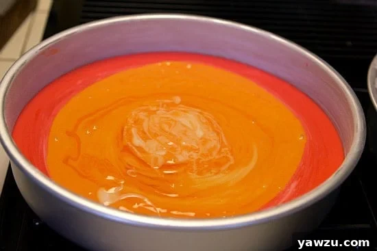 Orange cake batter slowly poured into the center of the red layer in a cake pan