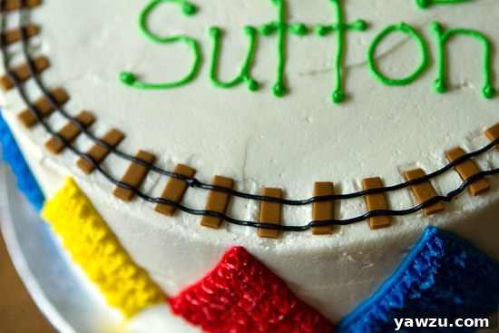 Close-up of a cake decorated with brown fondant train tracks and black icing rails