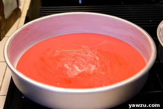 Red cake batter poured evenly into the bottom of a round cake pan