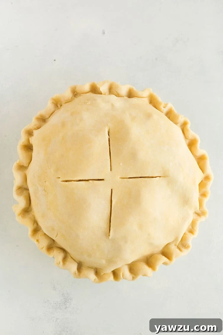 An assembled apple pie with a beautifully braided or crimped top crust, brushed with an egg wash and sprinkled with sparkling sugar, ready for baking.