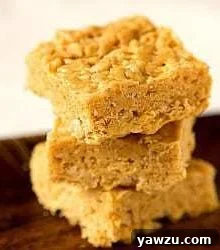 Stack of 3 peanut butter and white chocolate Rice Krispies treats on a wood board.