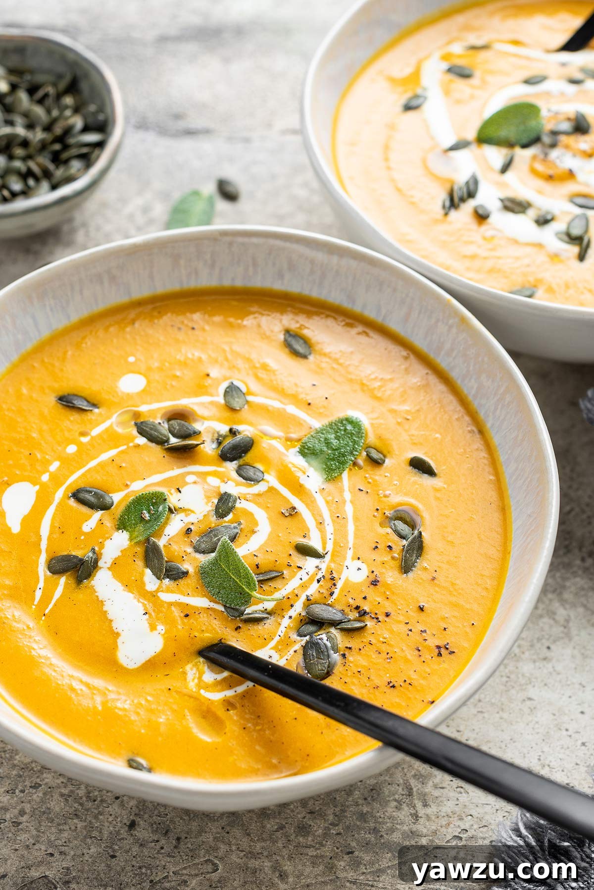 Bowl of pumpkin soup garnished with pumpkin seeds and sage leaves.