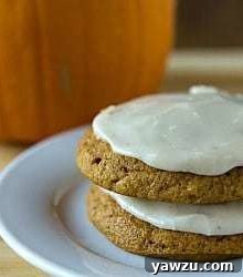 Stack of 2 pumpkin cookies topped with brown butter icing on a white plate.
