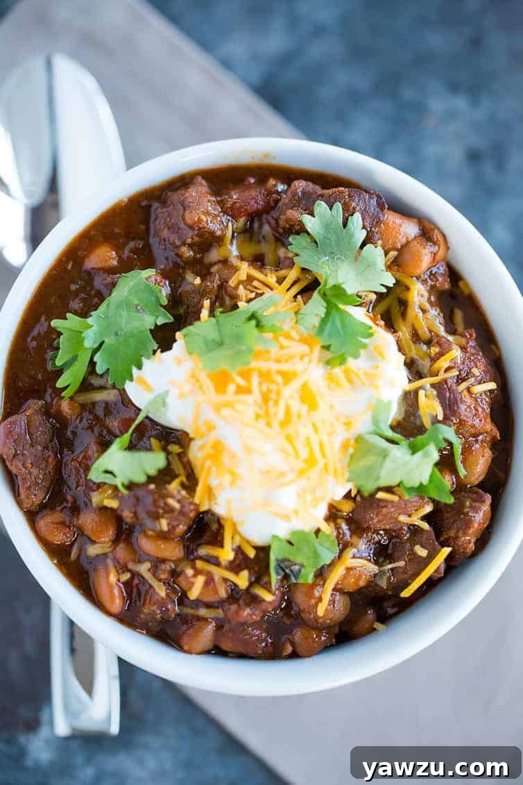 A beautifully presented bowl of homemade chili con carne, generously topped with fresh sour cream, shredded cheddar cheese, and vibrant cilantro, inviting hungry diners.