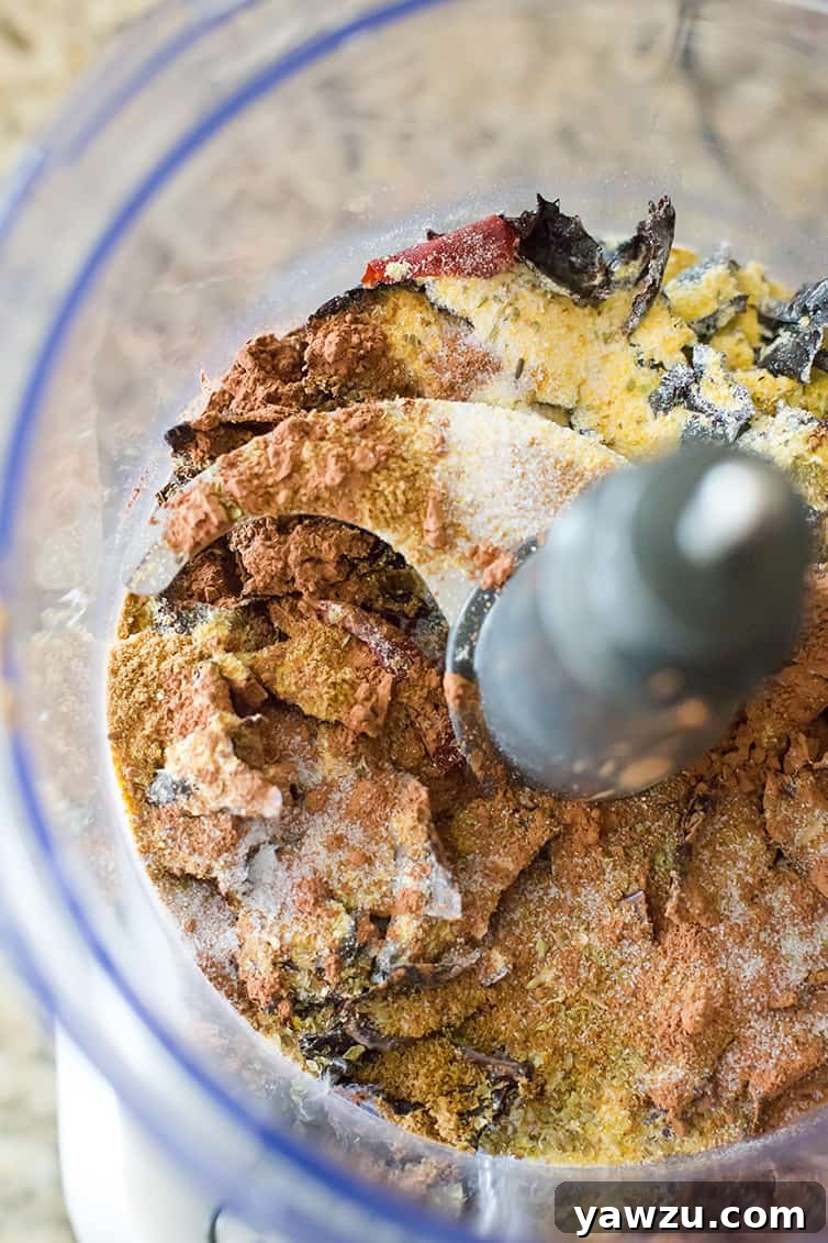 Various ingredients for the homemade chili paste, including toasted chiles and spices, positioned in a food processor bowl before blending.