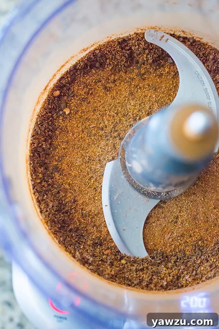 A close-up shot of finely ground homemade chili spice powder, showcasing its rich color and texture, inside a food processor bowl.