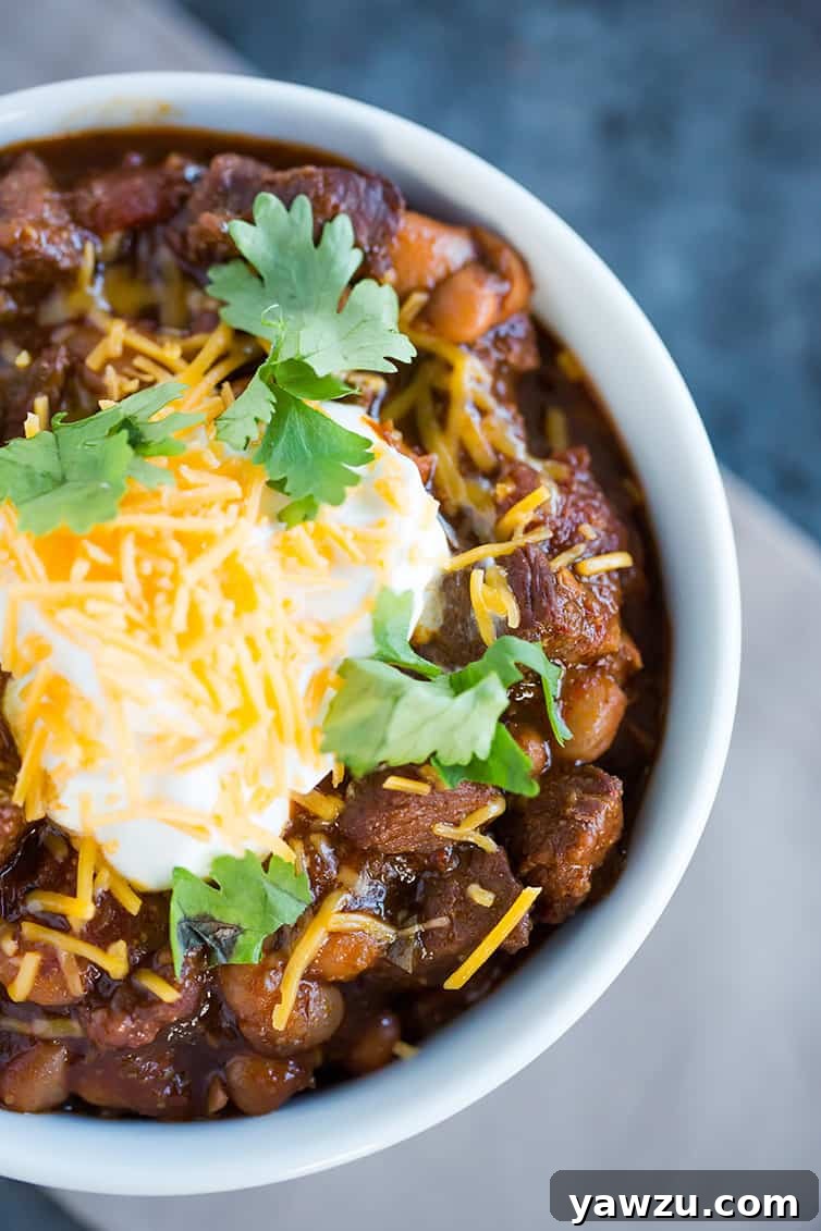 A close-up shot of a bowl of chili con carne, lavishly garnished with cool sour cream, golden shredded cheese, and fresh green cilantro on top, highlighting its appetizing appeal.