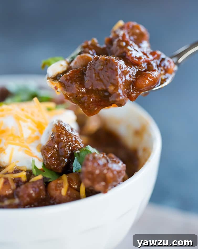 A big spoonful of chili con carne, generously filled with tender beef chunks and beans, being taken from the bowl, ready to be enjoyed.