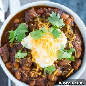 A bowl of chili con carne topped with sour cream, shredded cheese and cilantro.