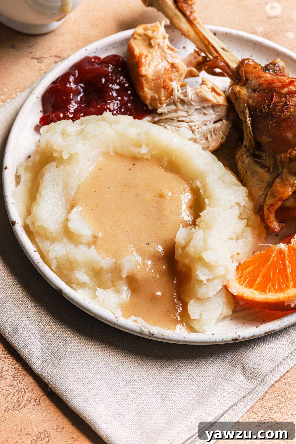 Plate of Thanksgiving food including turkey, cranberry sauce, mashed potatoes, and a generous serving of homemade make-ahead turkey gravy.