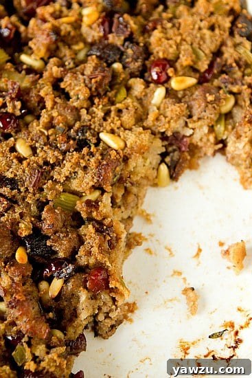 Close-up of a serving of Sausage, Fig & Cranberry Stuffing in a white bowl, garnished with fresh rosemary