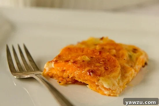 A serving of Sweet Potato Gratin with Gruyere on a white plate, showcasing the creamy layers and golden crust.