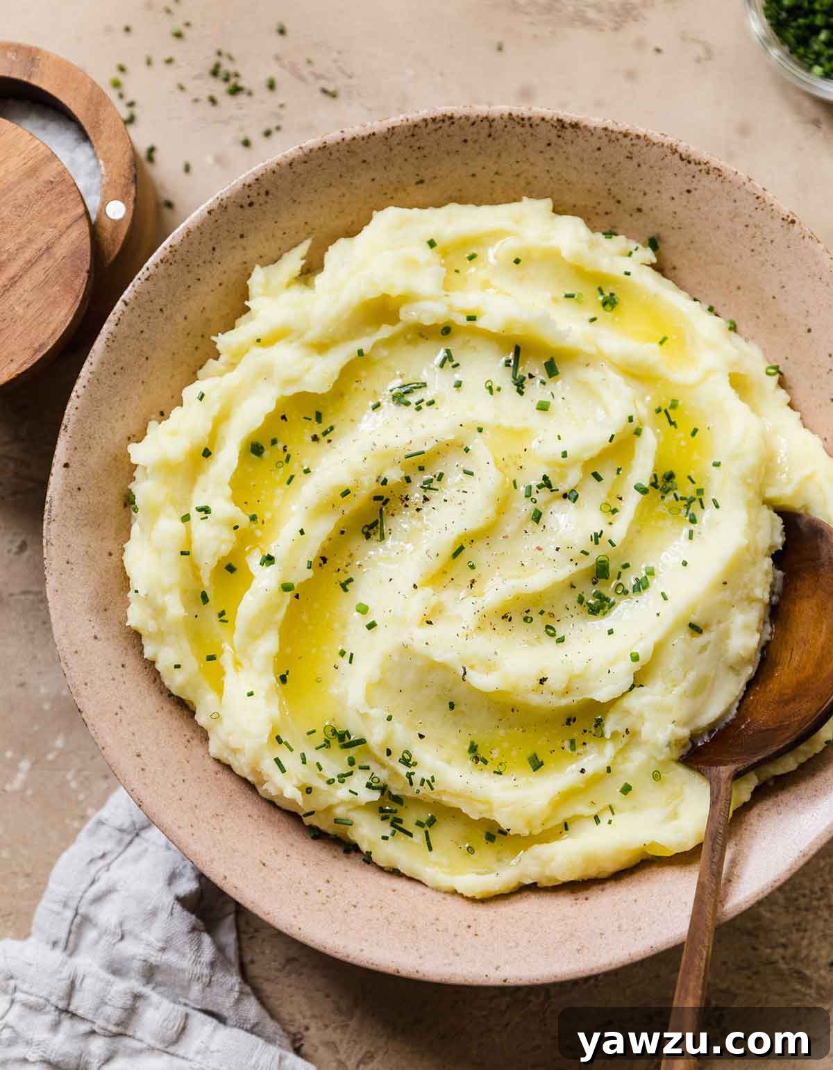 Overhead photo of pink rustic bowl full of mashed potatoes sprinkled with chopped chives and a wooden spoon nestled inside.
