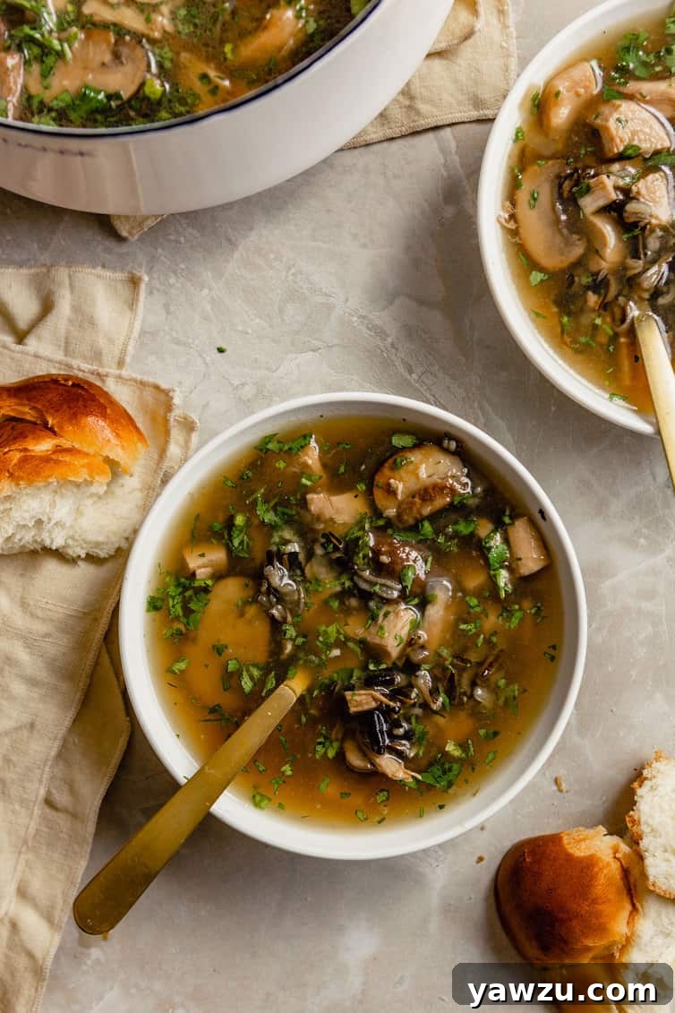 A bowl of turkey wild rice soup with bread and rolls on the side.