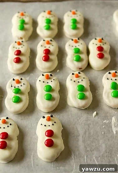 Close-up of a partially decorated Nutter Butter Snowman, showing the white chocolate coating and initial M&M button placement.