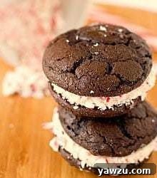 Stack of 2 chocolate peppermint whoopie pies on a wood board, garnished with candy canes.