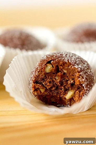 A close-up of a stack of chocolate bourbon balls, coated in sugar, on a white plate.