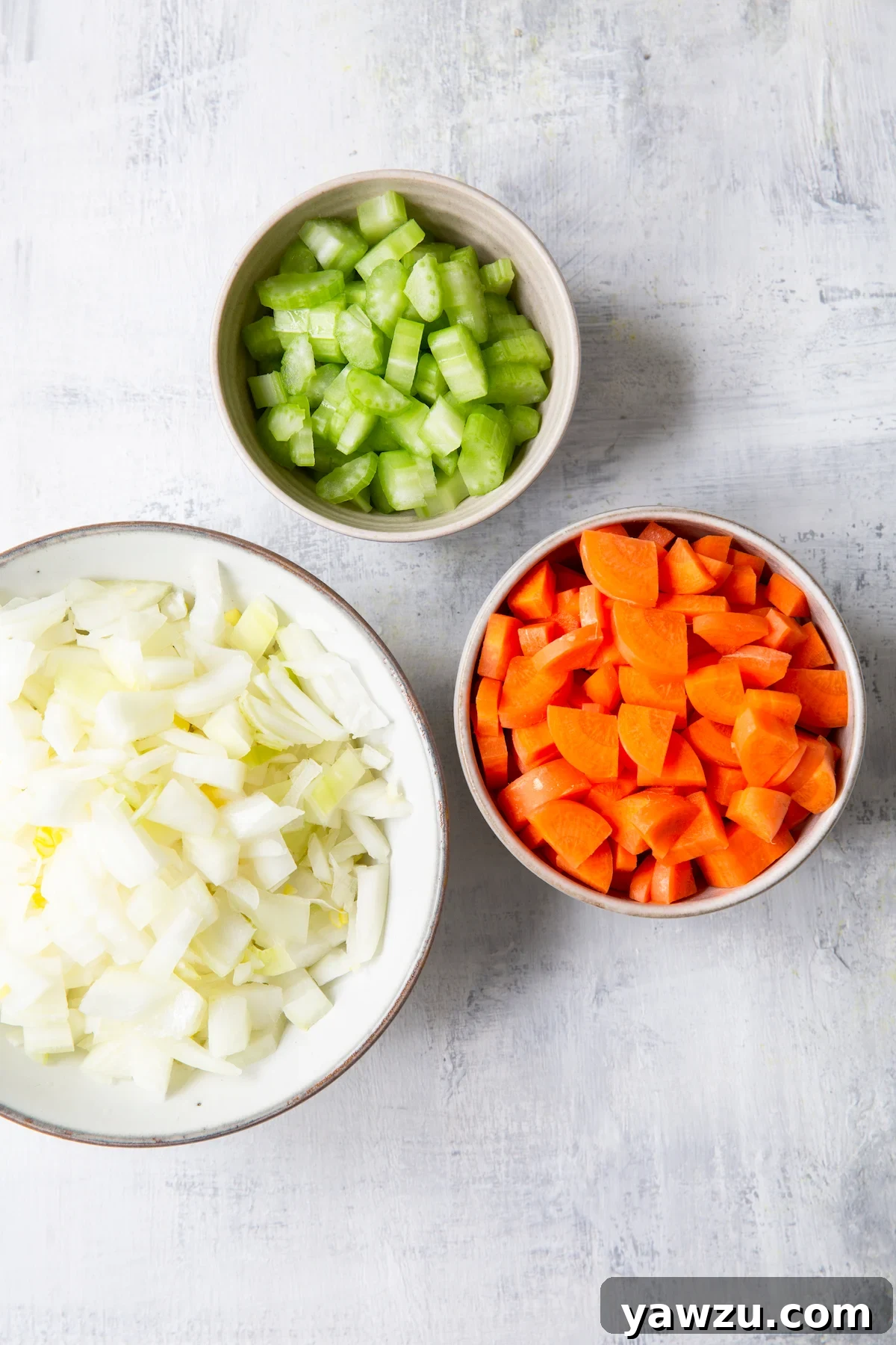 Overhead shot of diced onions, carrots, and celery in separate bowls