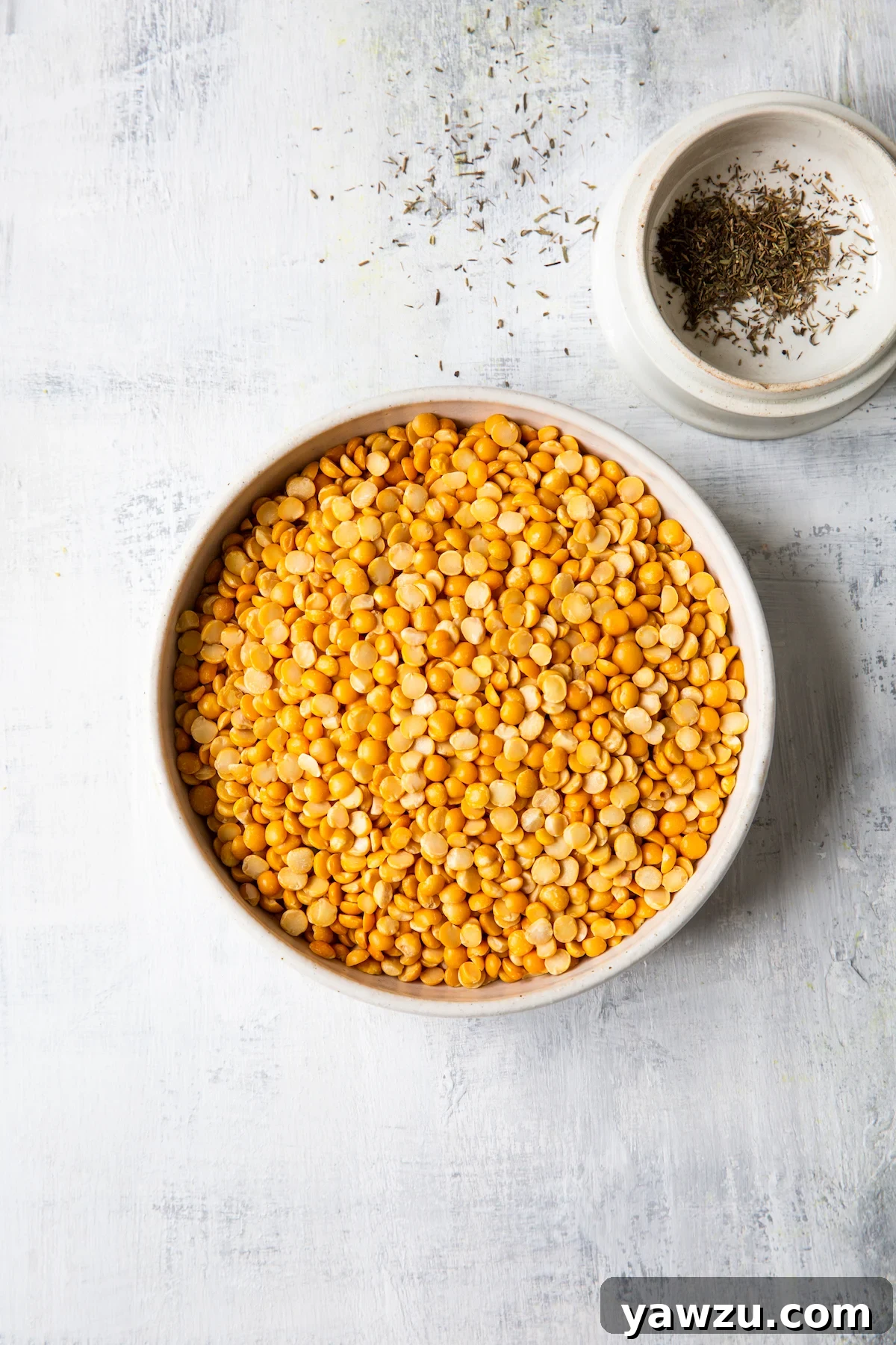 Overhead shot of yellow split peas in a bowl next to a small bowl of dried thyme