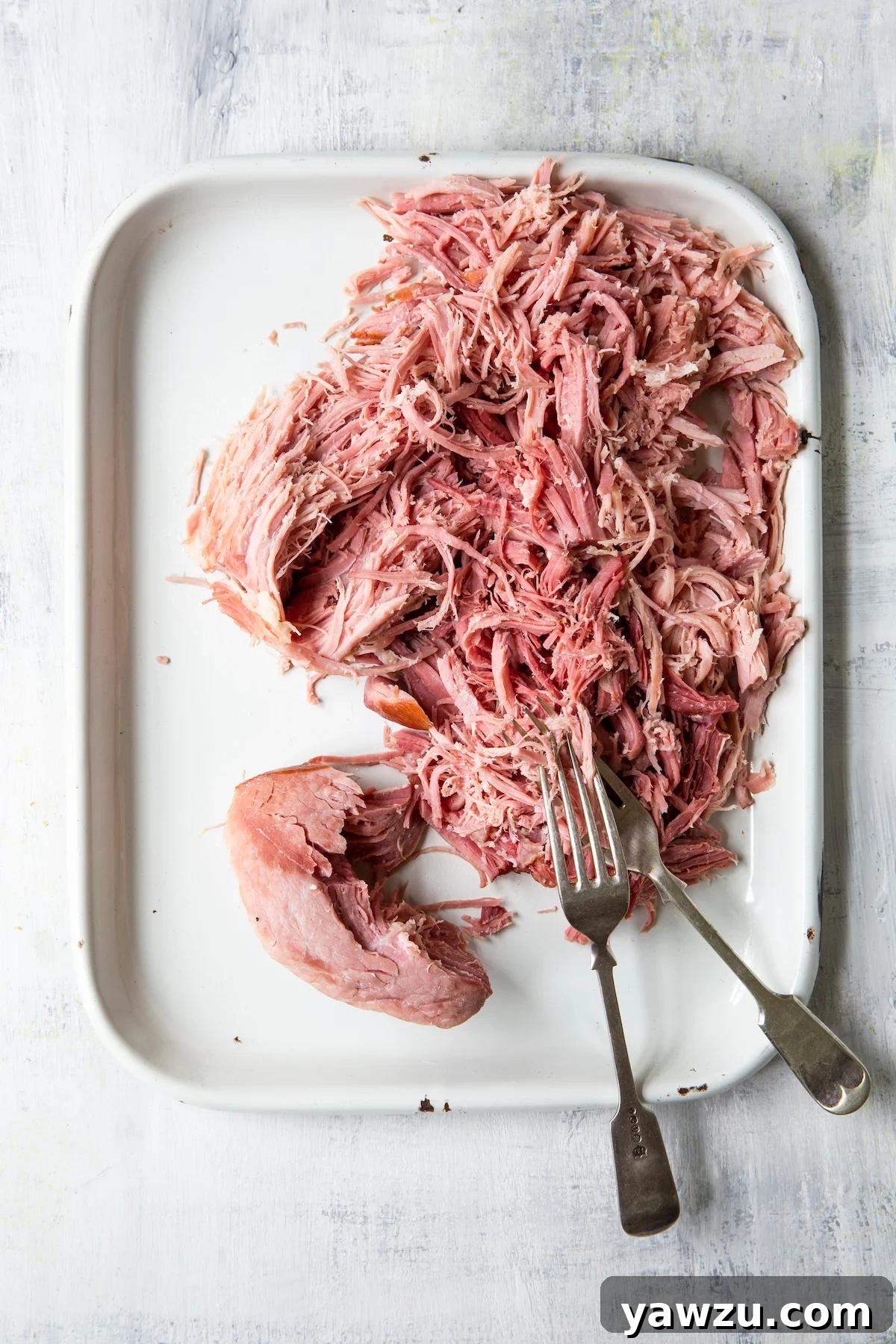 Overhead shot of ham being shredded on a platter with two forks