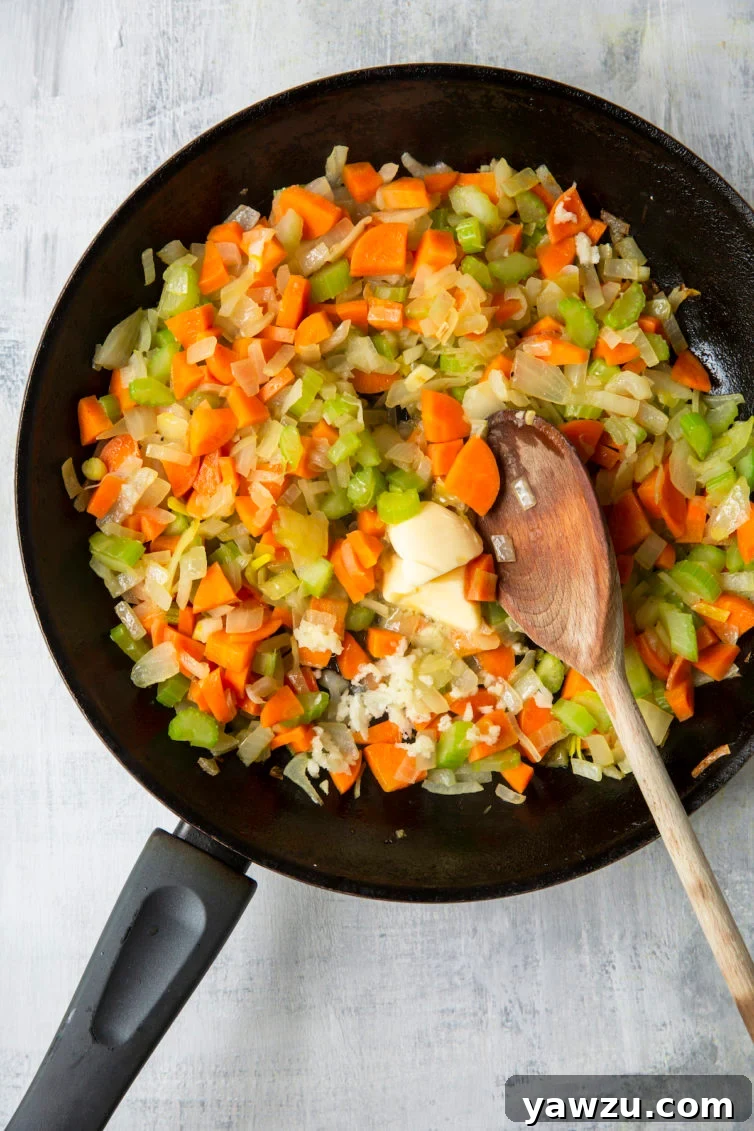 Diced onions, celery, and carrots in a skillet with a wooden spoon, beginning to brown