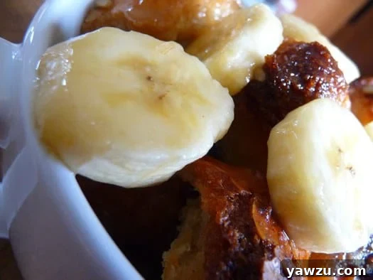 A stack of individual servings of Bananas Foster bread pudding, each topped with a delicate sauce, presented in white mugs.