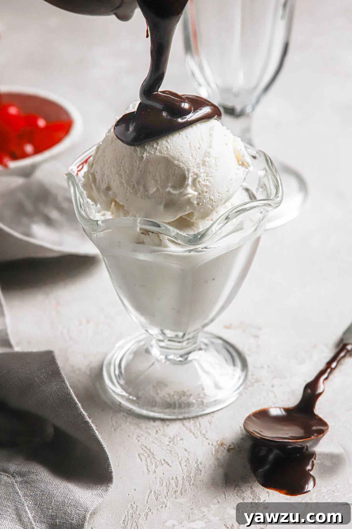 Vanilla ice cream in a parfait glass with warm hot fudge being poured generously on top, creating a luscious dessert.