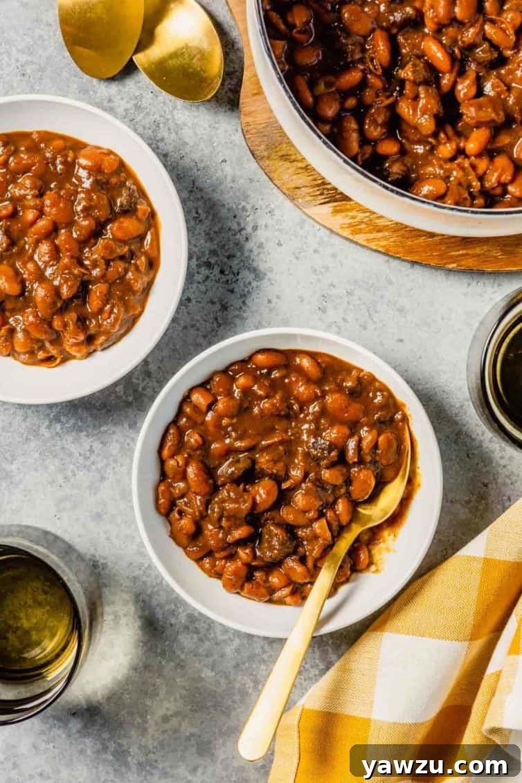 A white bowl with baked beans and a spoon on a grey counter, with another white bowl of beans in the background.