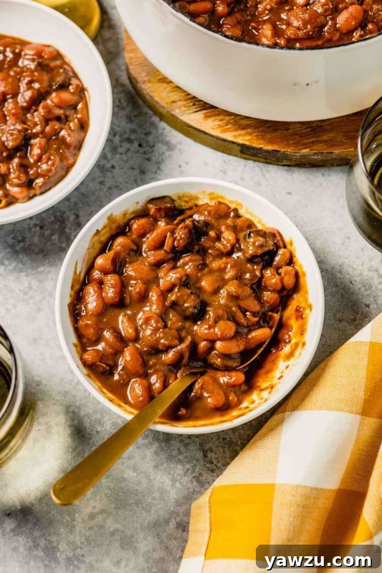 A white bowl with baked beans and a yellow and white buffalo check towel to the bottom left.