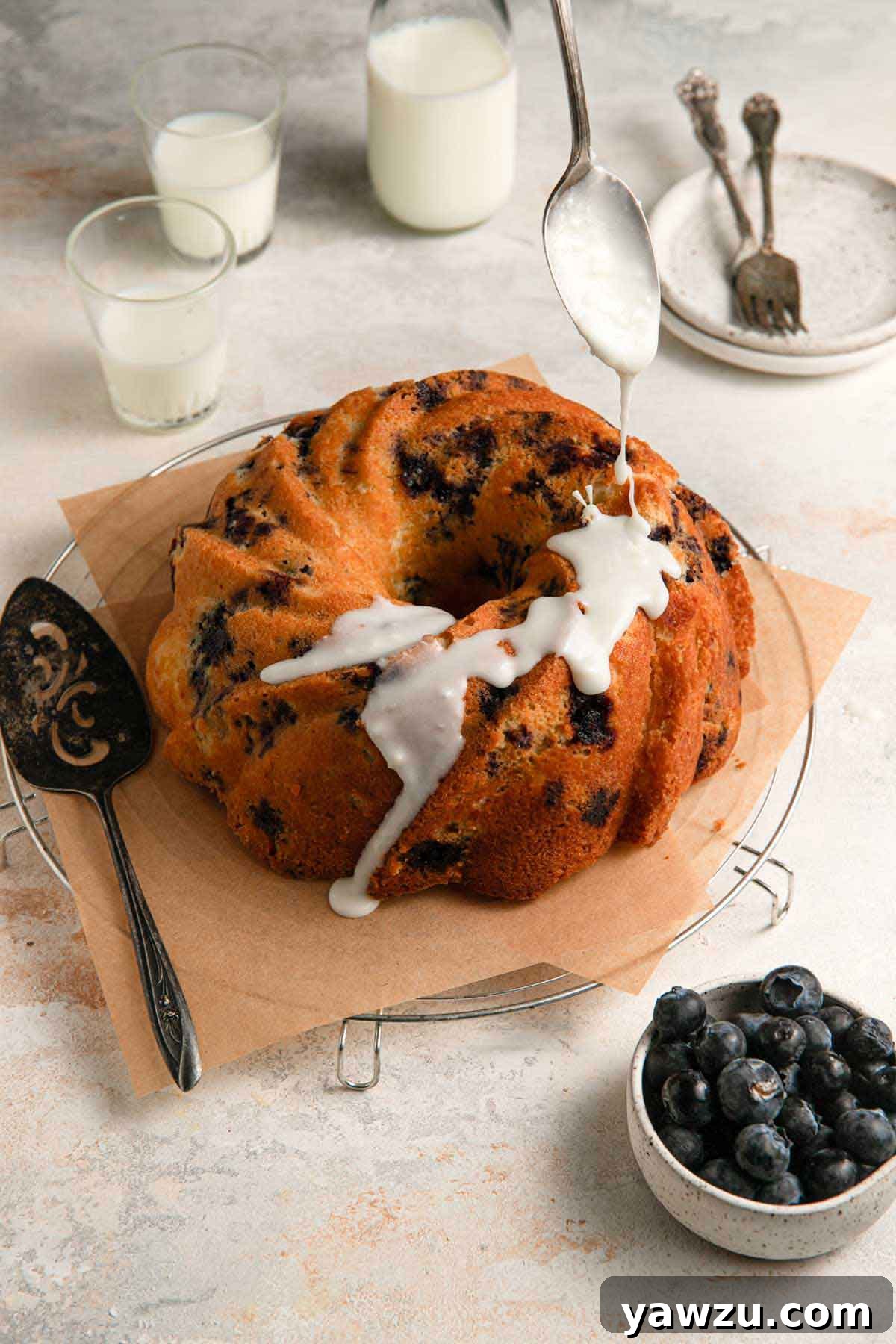 Icing being drizzled on a blueberry cake.