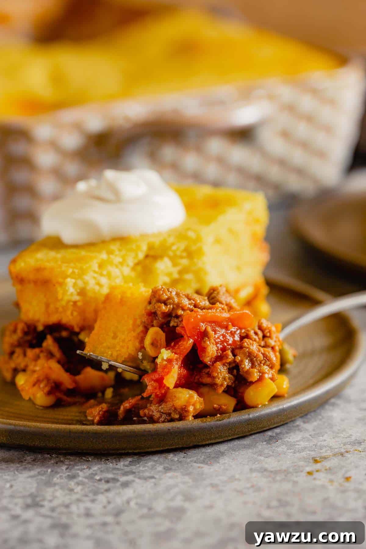 A slice of delicious Tamale Pie on a rustic brown plate, served with a fork, showing the distinct layers of cornbread and a rich ground beef filling.