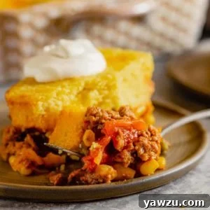 A square photo of a delicious slice of Tamale Pie on a brown plate, elegantly topped with a swirl of sour cream.