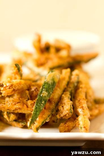 A hand reaching for a crispy beer-battered zucchini fry from a basket on a rustic table.