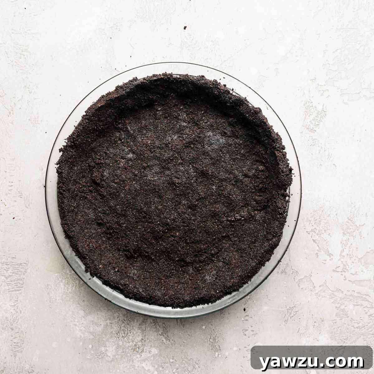 A perfectly formed Oreo cookie crumb crust, pressed firmly into a clear glass pie plate, ready for baking or chilling.