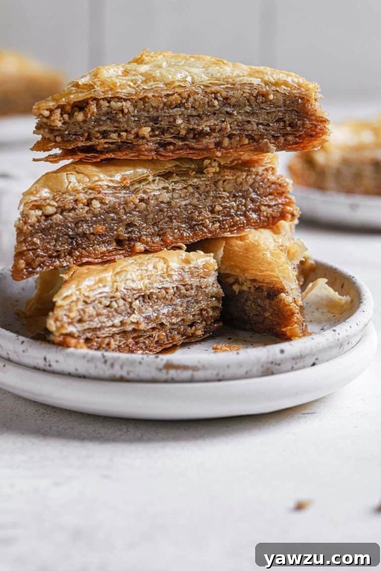 A stack of golden baklava triangles on white plates, glistening with syrup.