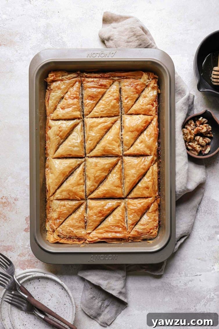 A top-down photo of baklava on a counter, accompanied by a dish towel and a small bowl of walnuts.