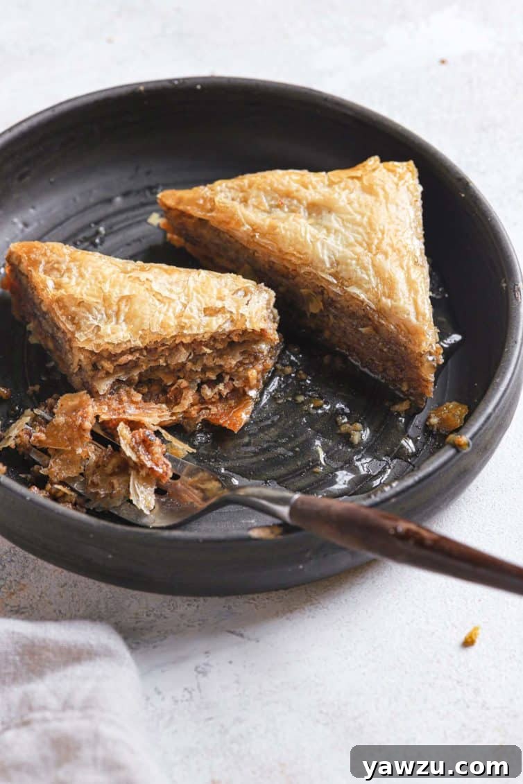 Two baklava triangles elegantly placed on a black plate with a fork beside them.